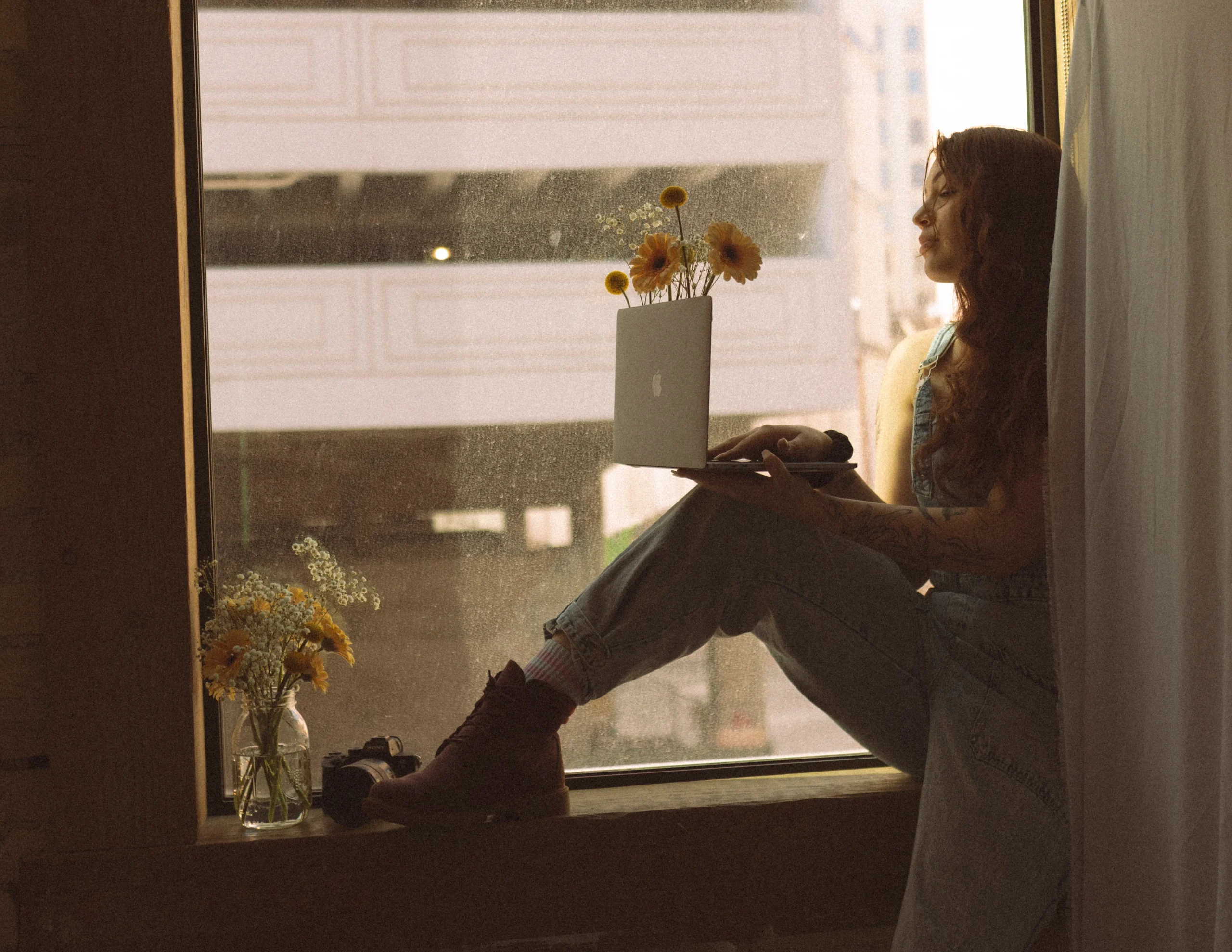 Mica sitting in windowsill with laptop and flowers