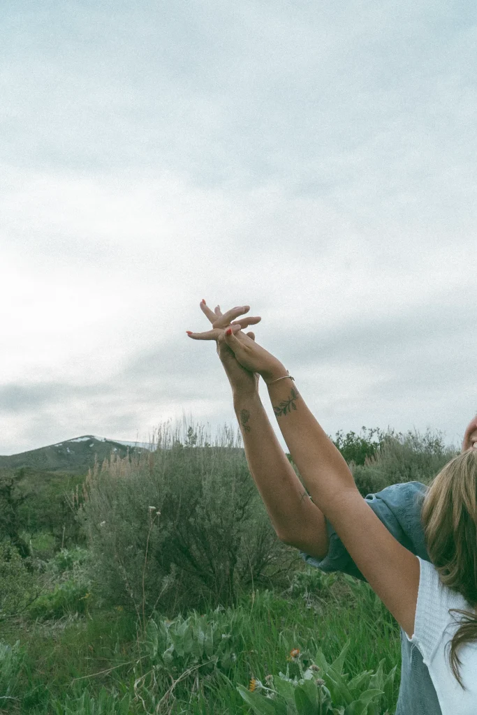 Hands intertwined and lifted toward the sky in a grassy mountain landscape.