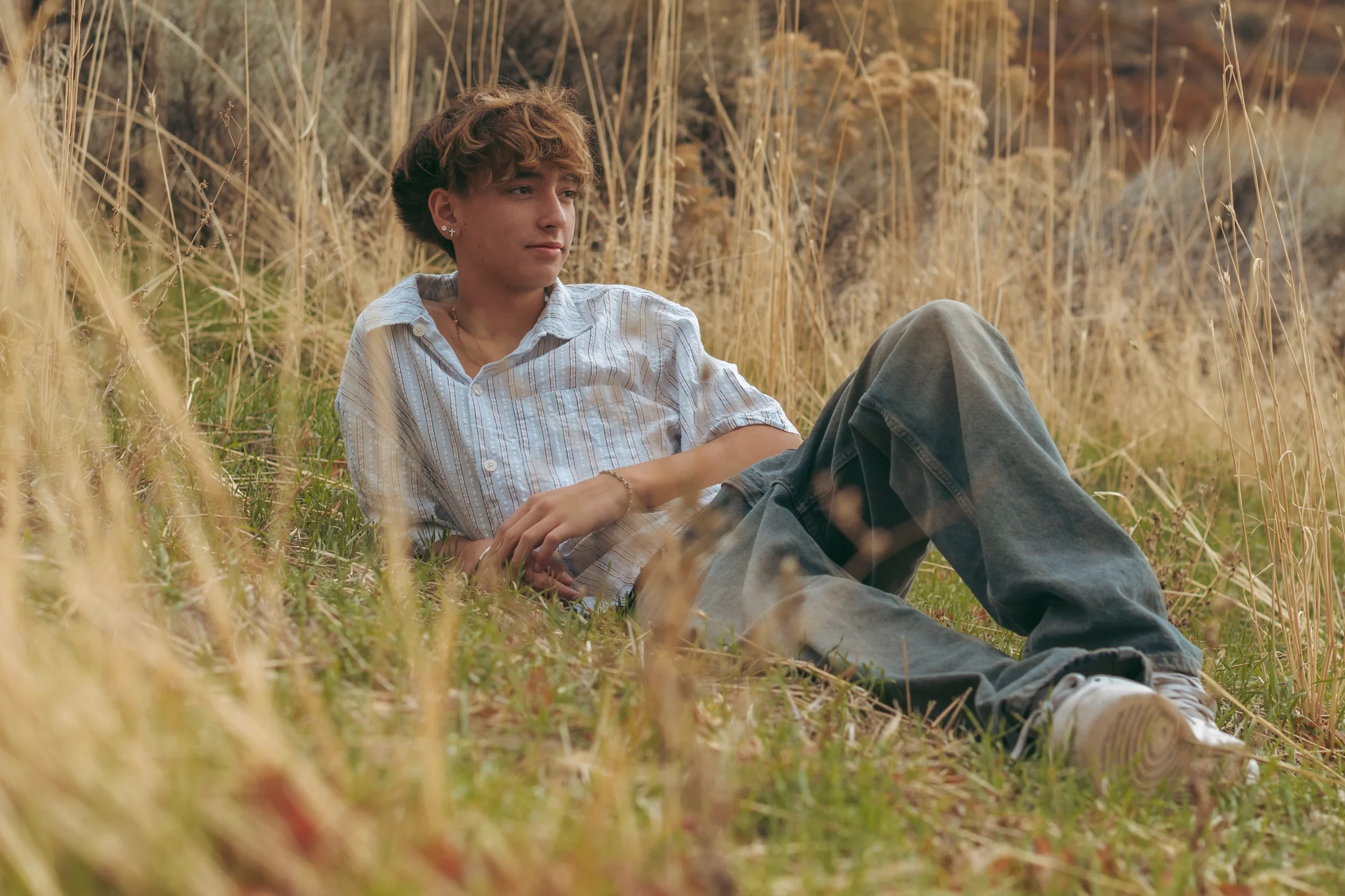 Teen boy reclining in a field of tall golden grasses, gazing into the distance.