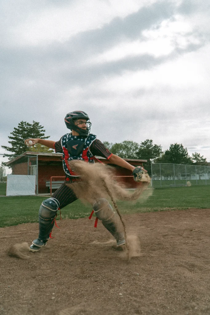 Catcher throwing ball with dirt flying on a baseball field.
