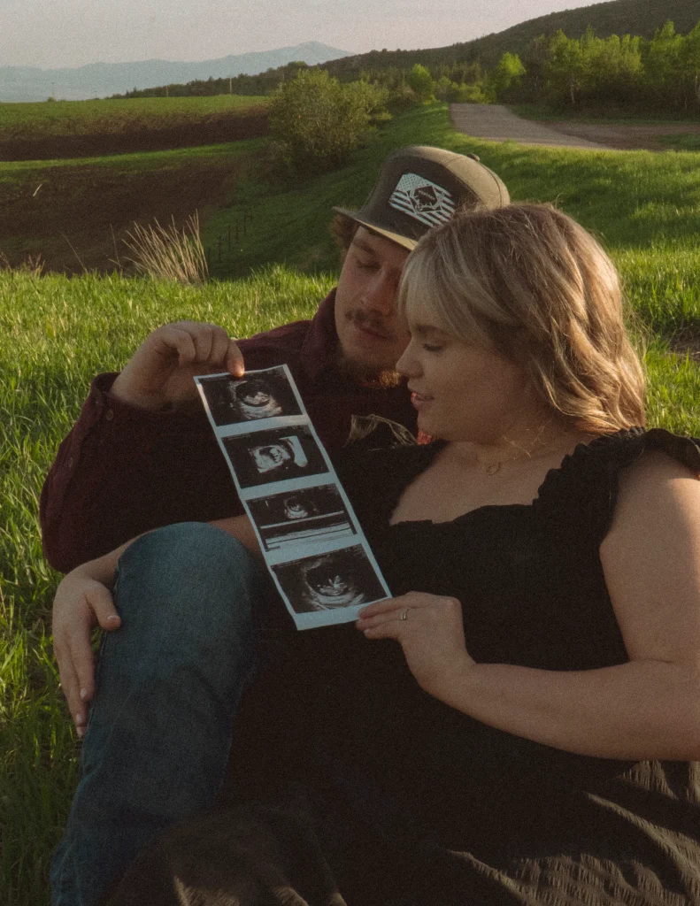 Couple sitting in a grassy field looking at ultrasound images together.