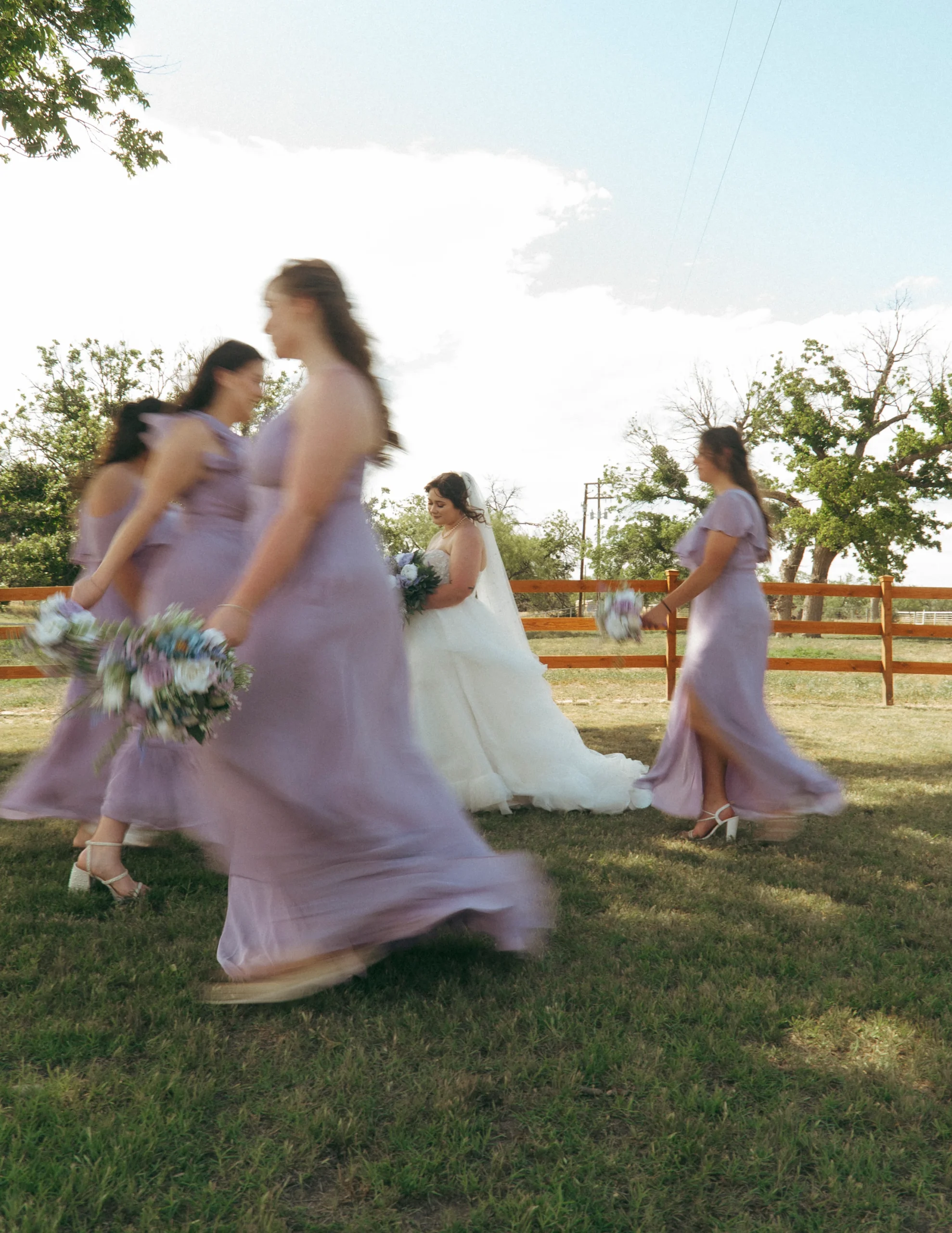Bridesmaids in lavender dresses walking around bride as she smiles, creating motion blur.