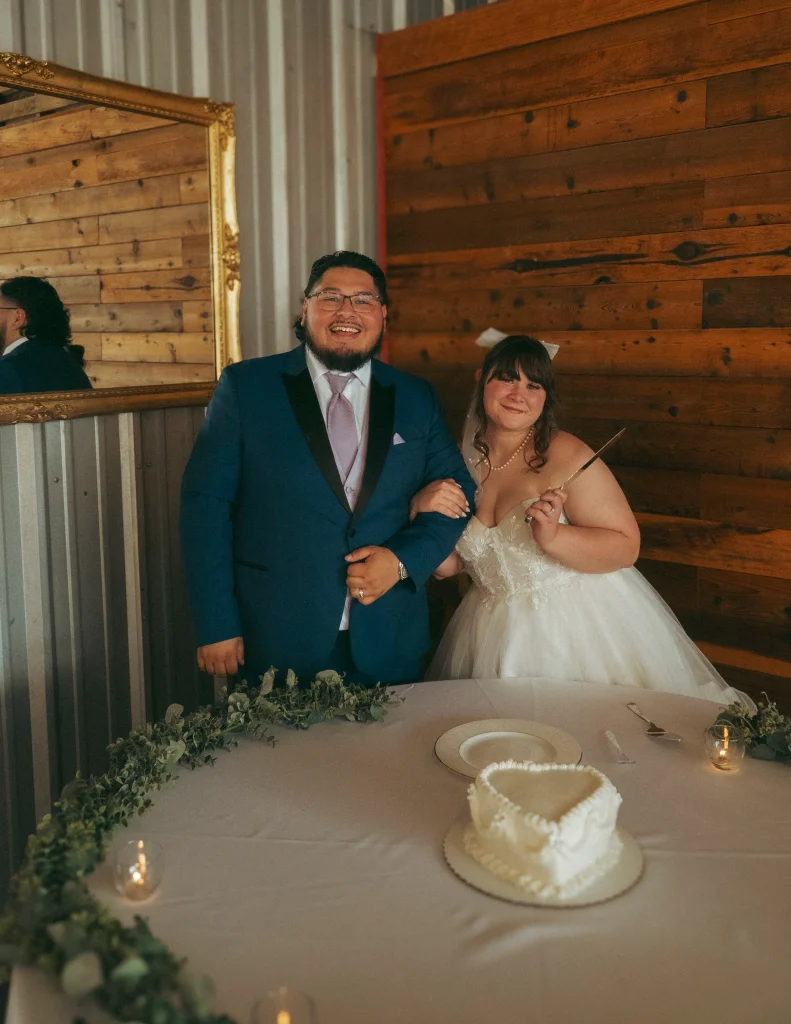 Bride and groom standing together at their cake table, smiling and posing before cutting the wedding cake.