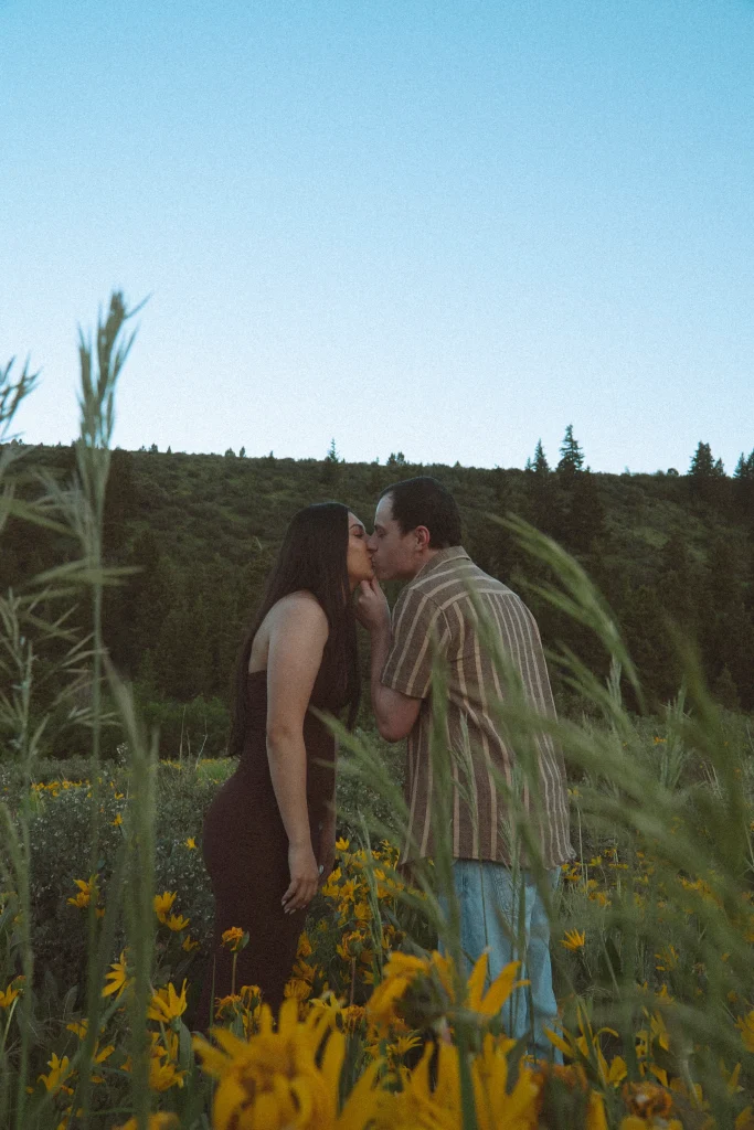 Couple shares a kiss in a field of yellow wildflowers at sunset.