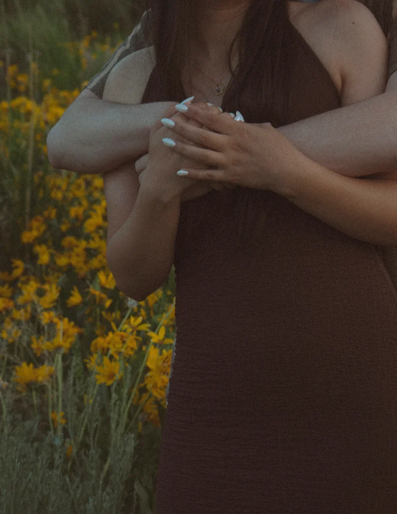 Close-up of couple holding hands in a field of yellow flowers.