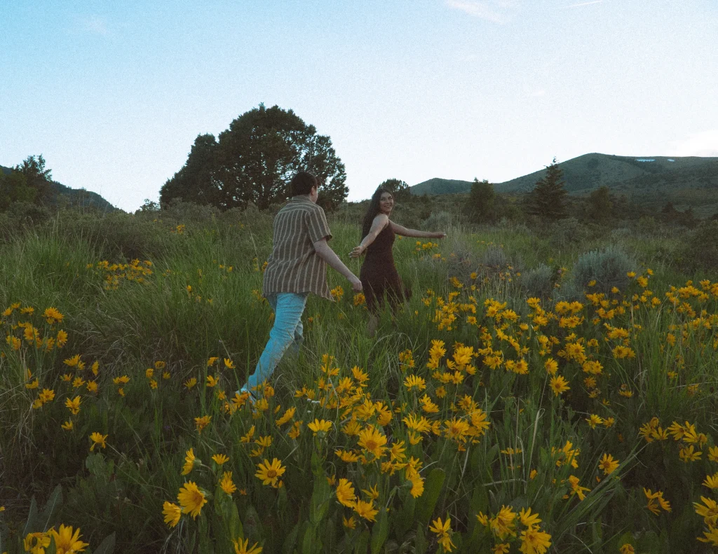 Couple runs hand-in-hand through a field of yellow wildflowers.