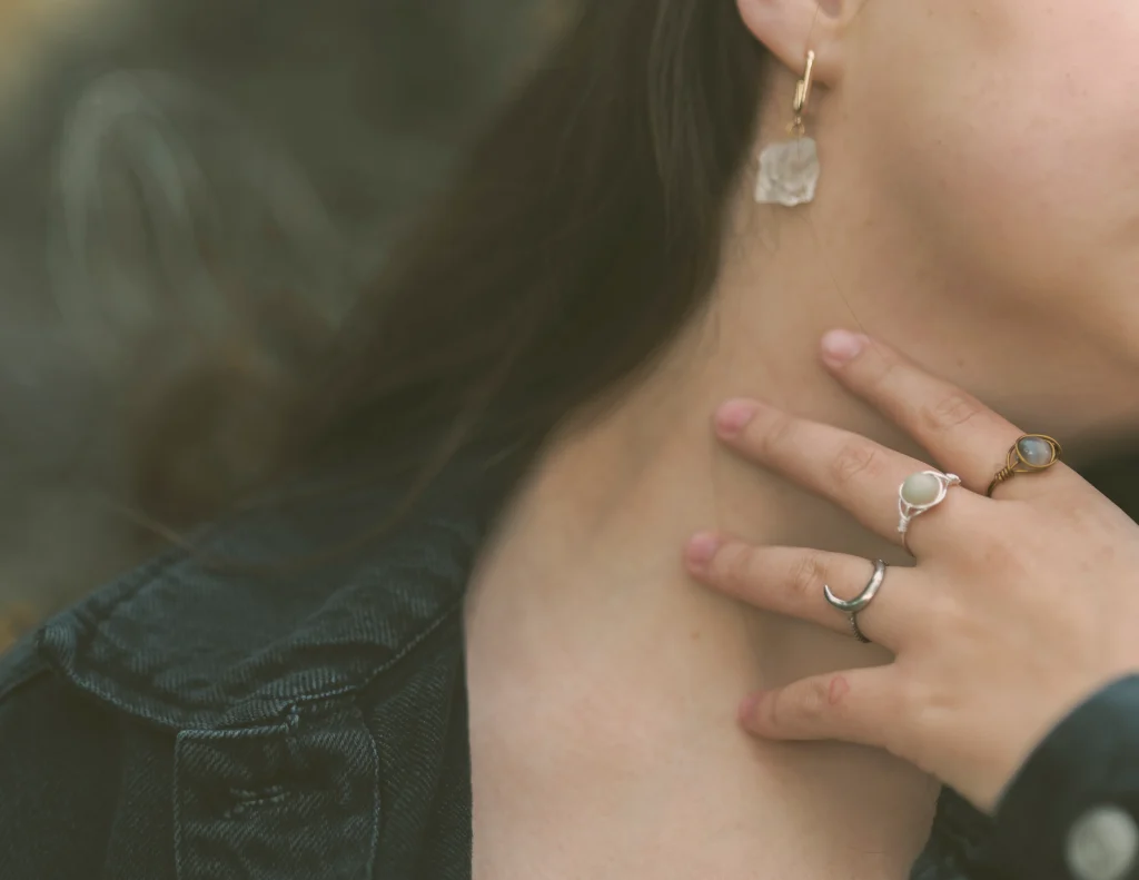 Close-up of hands holding a black denim jacket, showcasing multiple rings and a finger tattoo.