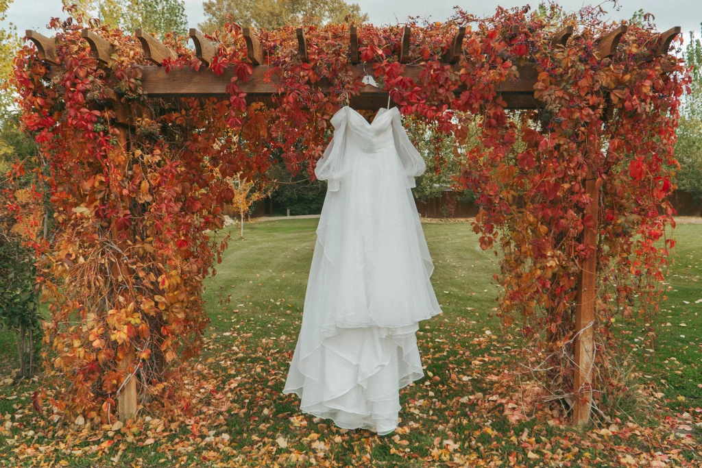Wedding dress hanging from a wooden arbor covered in bright red autumn leaves.