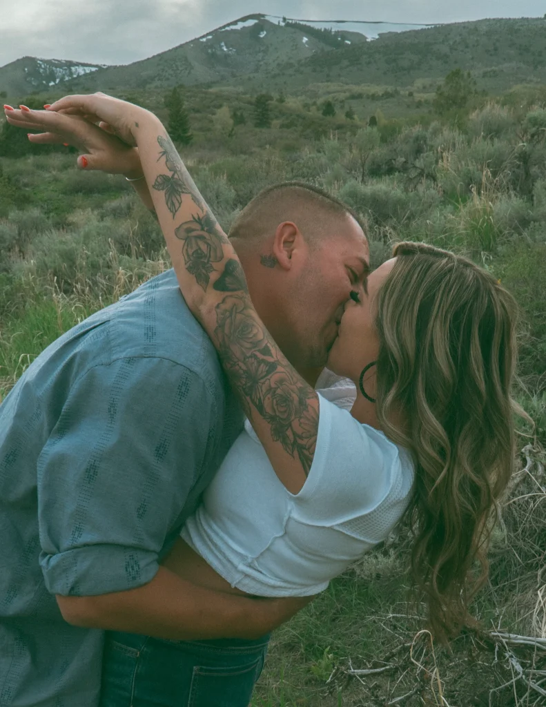 Man dips woman backward as they kiss in a mountain meadow.