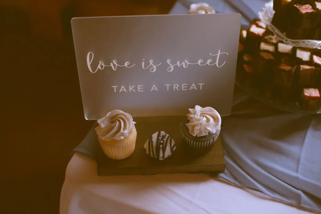 Wedding dessert display with cupcakes and a sign reading “Love is sweet, take a treat.”