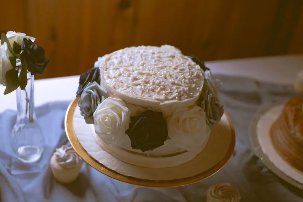 White wedding cake decorated with black, gray, and white faux roses around the base.