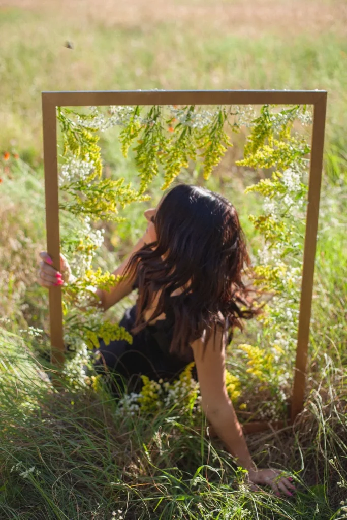Woman in a black dress leaning back inside a flower-decorated frame in a grassy field.