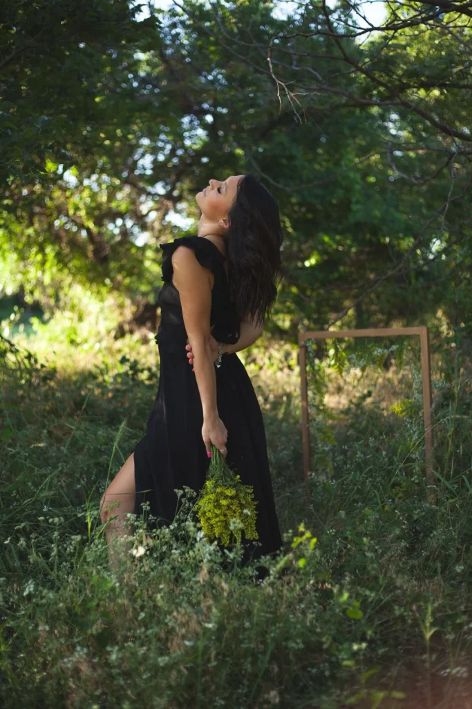 Woman in a black dress leaning back inside a flower-decorated frame in a grassy field.
