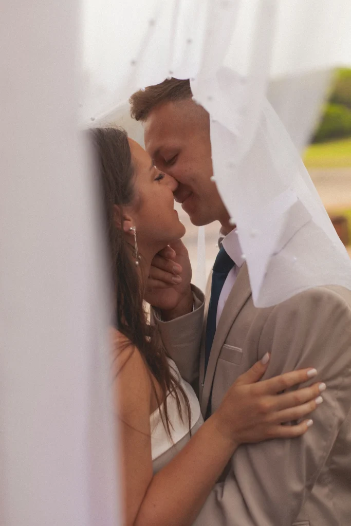 Bride and groom kissing on stone steps of a historic building, with the bride’s long veil trailing behind her.