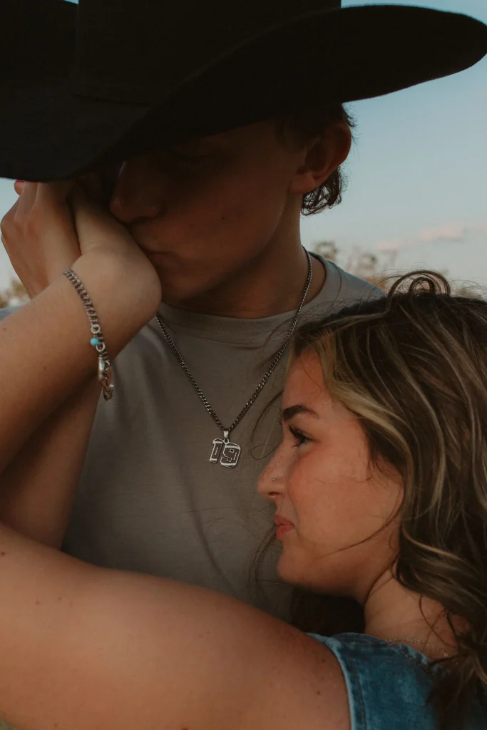 Close-up of man kissing woman’s hand as she leans against him, both wearing casual outdoor clothing.