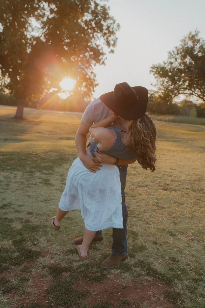 Man dipping woman for a kiss in a sunlit field during golden hour.
