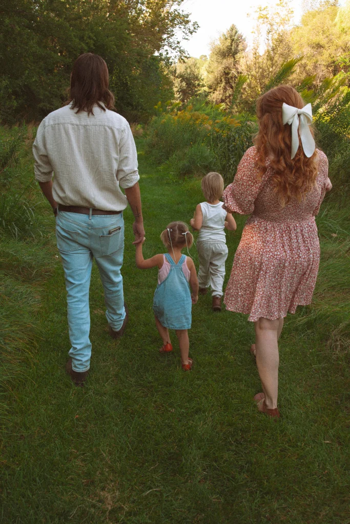 Family walking together on a grassy path surrounded by trees.