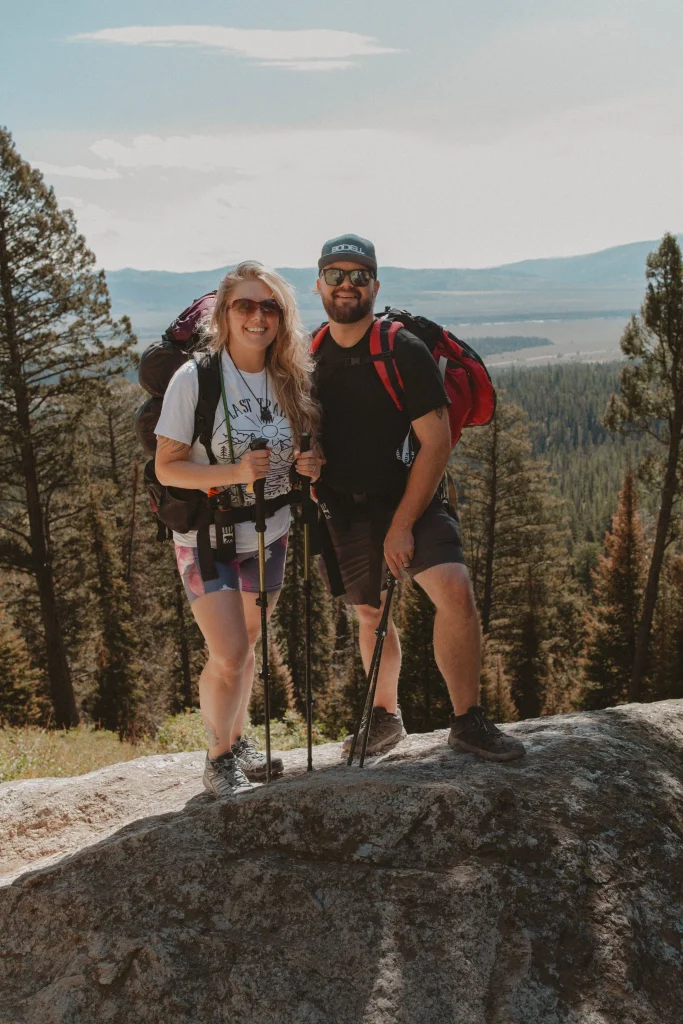 Couple posing together on a mountain overlook while hiking with trekking poles.