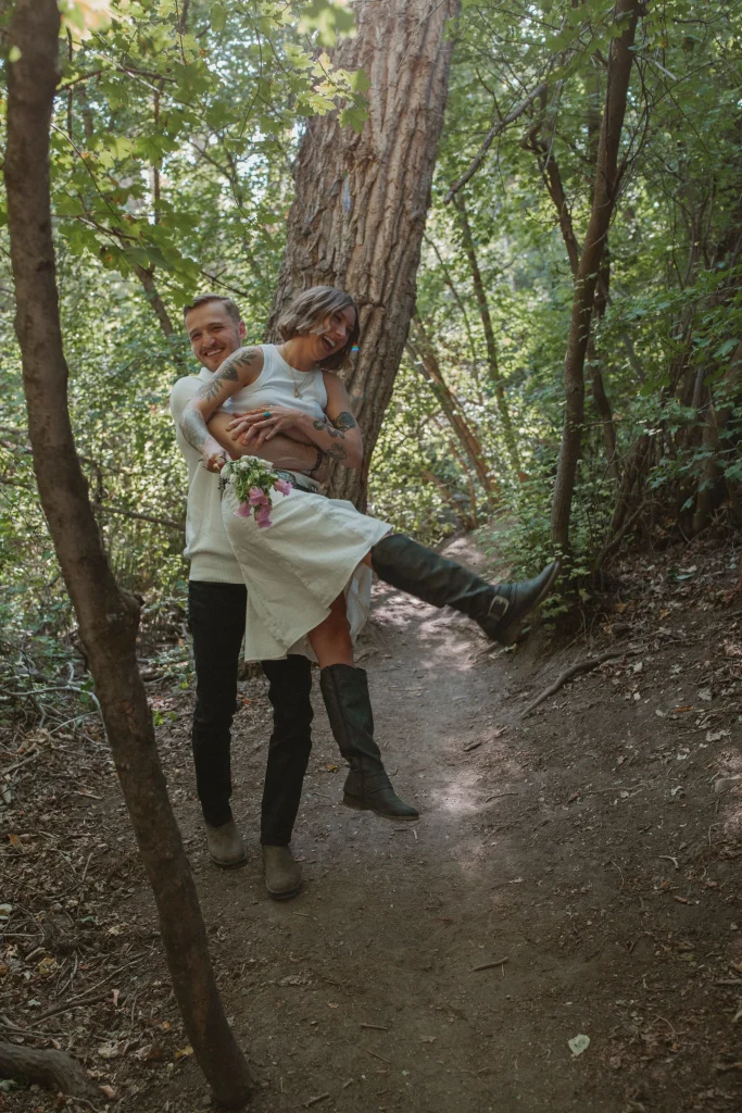 Man lifting laughing woman on a forest path as she holds flowers.