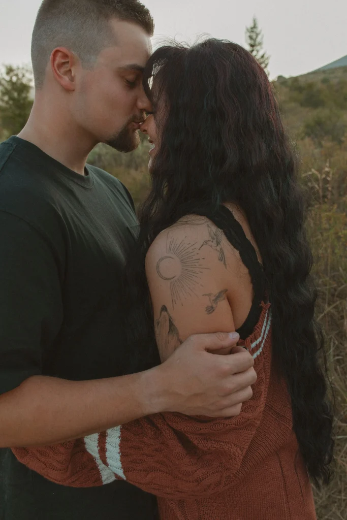 Close-up of a couple touching foreheads and smiling softly in a field at sunset.