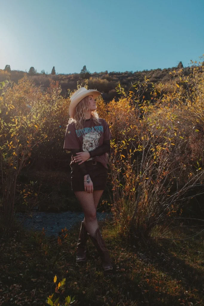 Woman in a cowboy hat posing in golden fall foliage under a clear blue sky.
