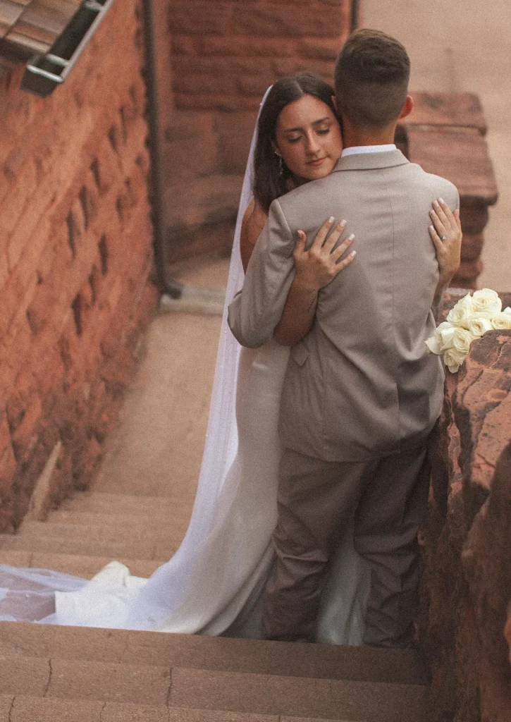 Bride and groom embracing on stone steps, bride’s veil flowing behind them.