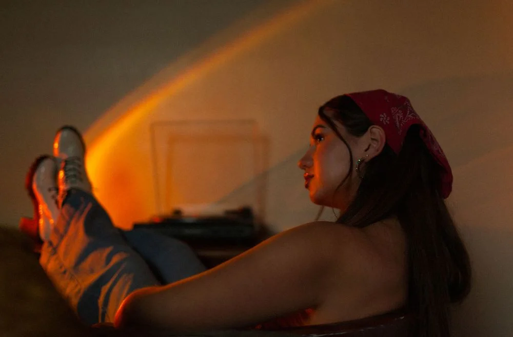 Side view of a woman lounging with her feet up, illuminated by warm light, with a record player in the background.