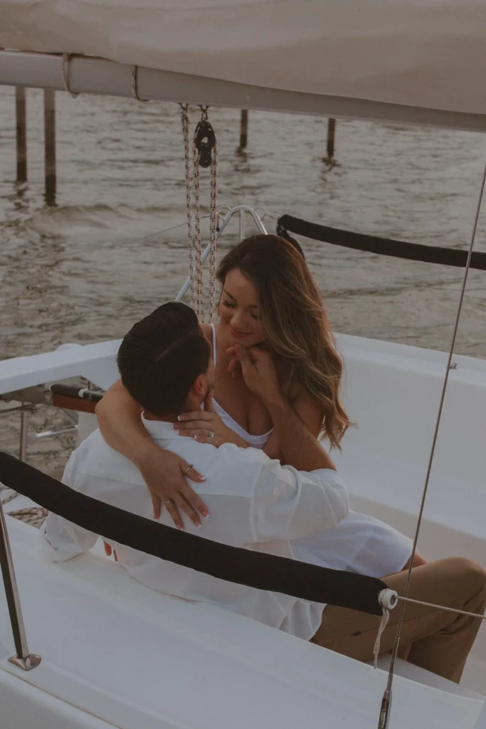Woman sitting on a man’s lap as they relax together on a sailboat, smiling softly.