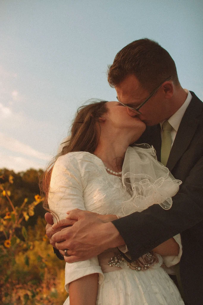 Groom kissing bride at sunset as she tilts her head back in a lace wedding dress.