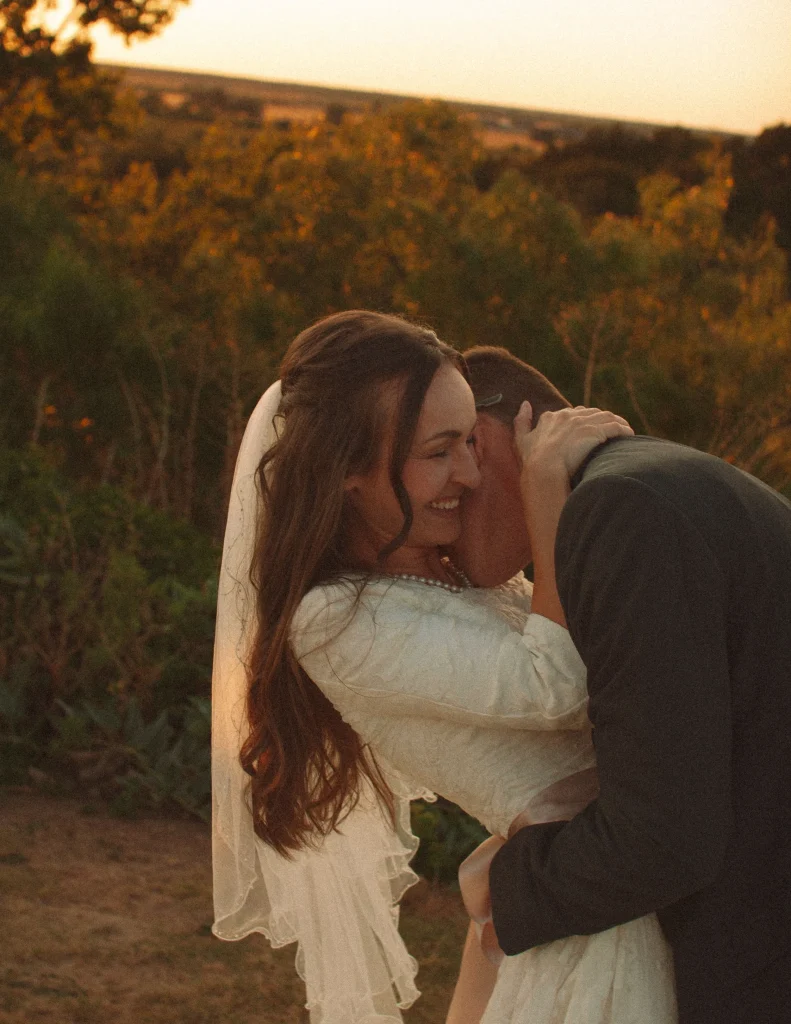 Bride laughing as groom leans into her during a playful wedding moment at sunset.