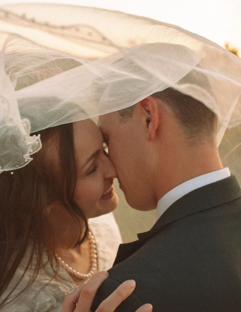 Bride and groom sharing a kiss under the bride’s veil during sunset.
