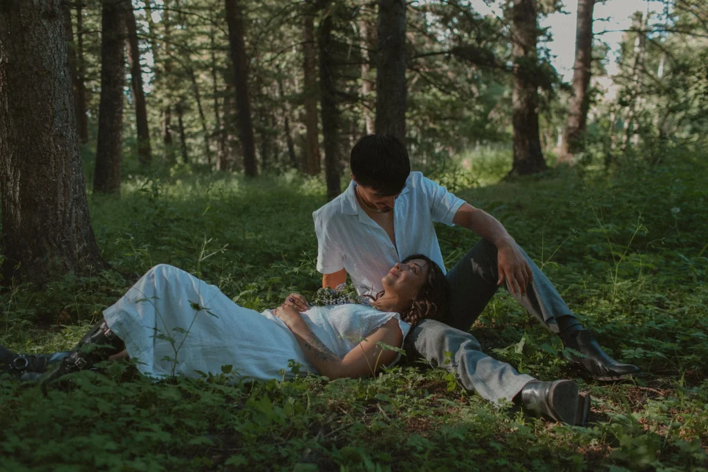 Woman rests in her partner’s lap on the forest floor, both looking at each other peacefully.