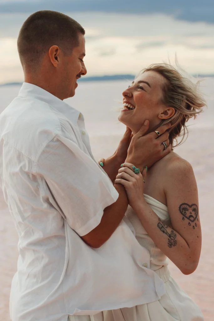 Couple laughing and holding each other on a pink salt flat.