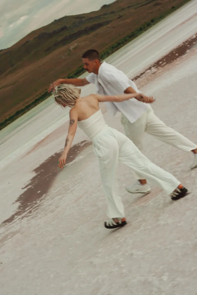 Couple running hand-in-hand across a salt flat wearing white outfits.