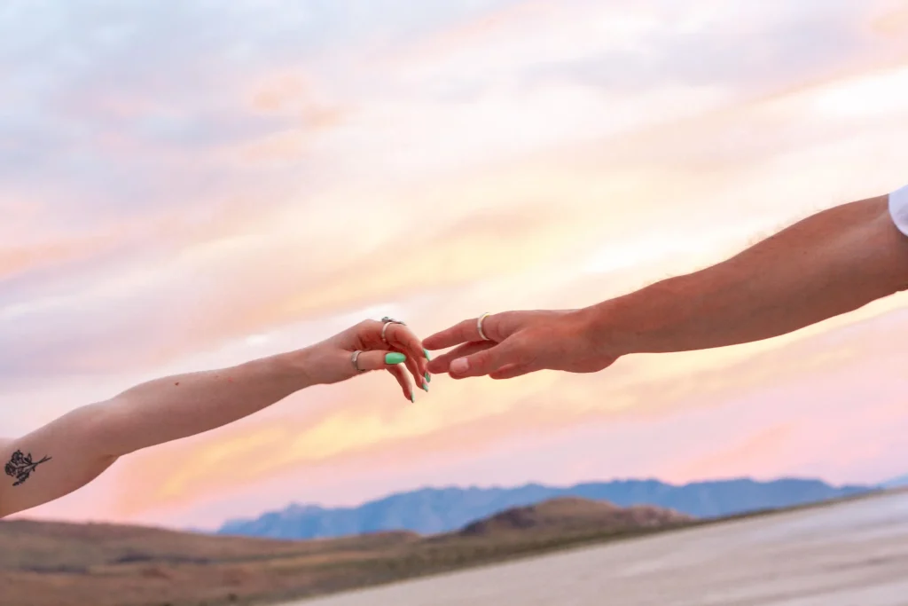 Close-up of two hands reaching toward each other at sunset in the desert.